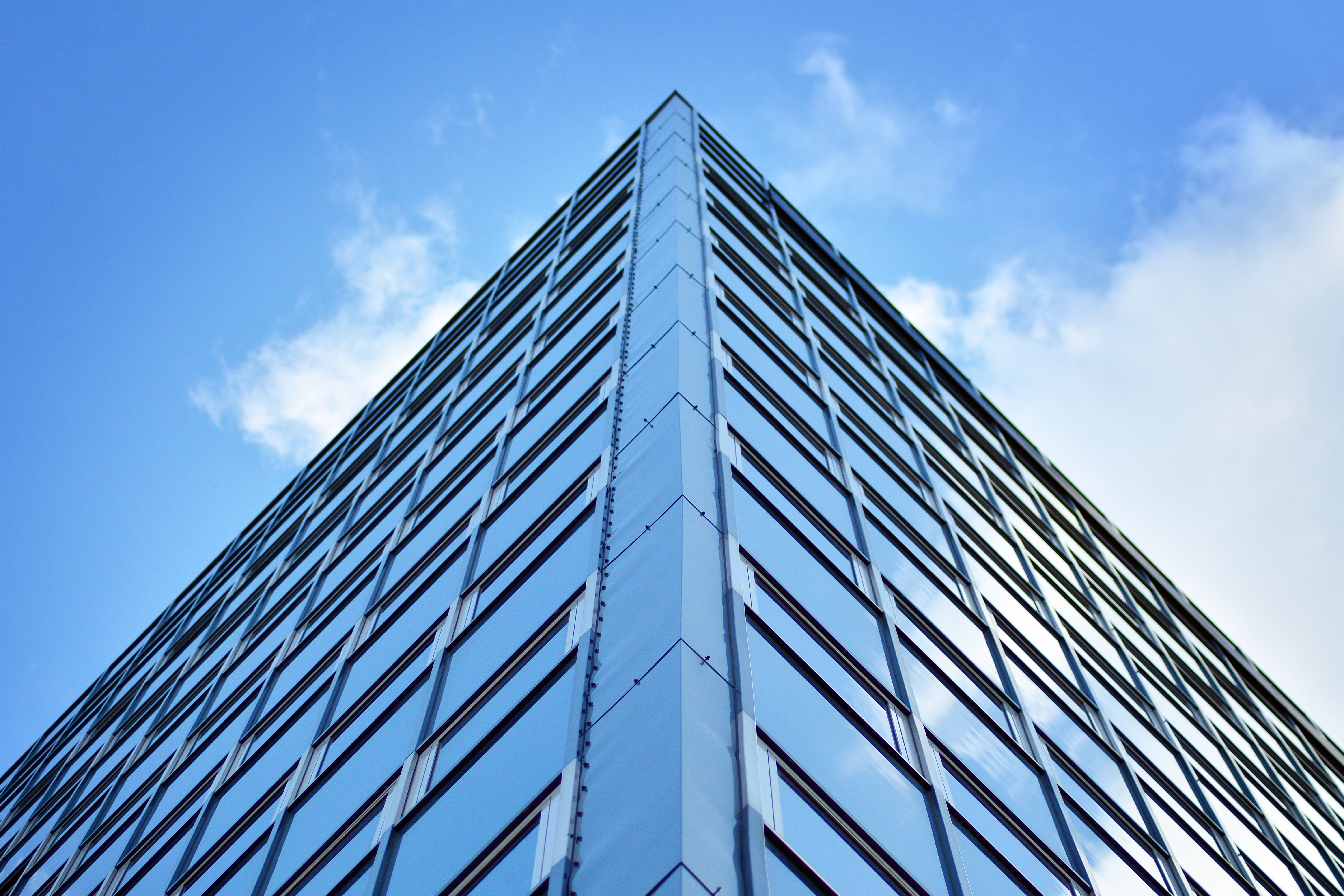 Blue wash image of a glass building with a blue sky with clouds in the background